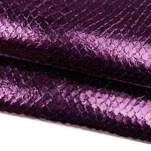 Op de afbeelding: Close-up van een getextureerd, metallic paars materiaal. Het oppervlak heeft een schubbenachtig patroon, met een glanzende glans die licht reflecteert. Het materiaal is gevouwen en onthult lagen en schaduwen.