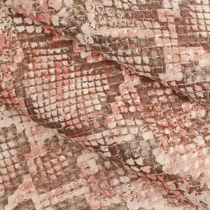 Peut inclure: Gros plan sur un tissu textur&eacute; avec un motif peau de serpent. Le motif pr&eacute;sente une grille carr&eacute;e r&eacute;p&eacute;titive dans des tons de rose, de marron et de blanc cass&eacute;. Le tissu semble pli&eacute;, cr&eacute;ant des ombres et de la profondeur.