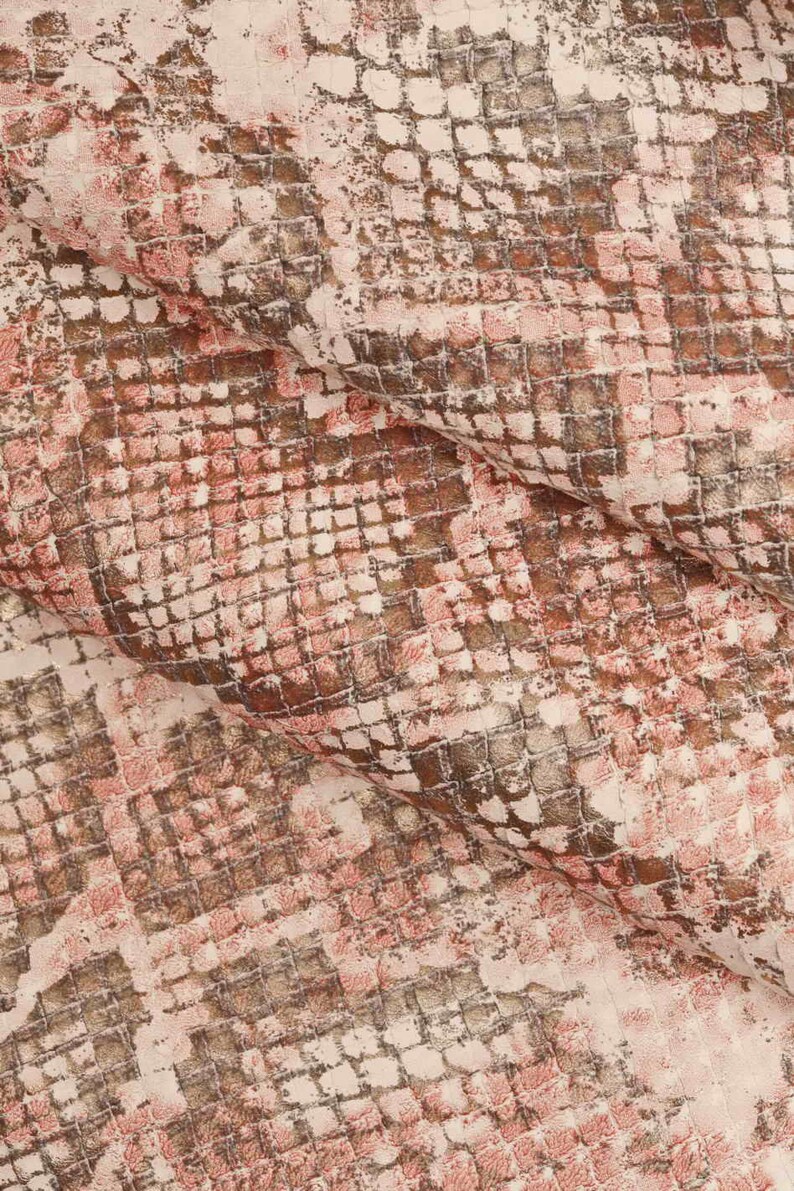 Peut inclure: Gros plan sur un tissu textur&eacute; avec un motif peau de serpent. Le motif pr&eacute;sente une grille carr&eacute;e r&eacute;p&eacute;titive dans des tons de rose, de marron et de blanc cass&eacute;. Le tissu semble pli&eacute;, cr&eacute;ant des ombres et de la profondeur.