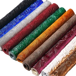 Pode incluir: Uma coleção de folhas de couro em relevo enroladas em várias cores. As cores incluem preto, azul, prata, vermelho, verde, laranja, castanho, roxo, branco e dourado. Cada folha apresenta um padrão floral detalhado.