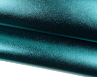 Puede incluir: Primer plano de una tela doblada de color verde azulado. El material tiene un brillo sutil, reflejando la luz y creando reflejos y sombras. La textura parece suave con ligeras variaciones.