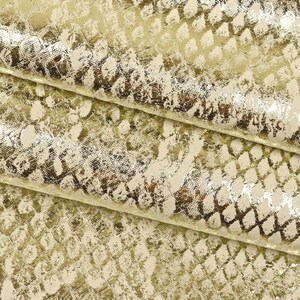 Könnte beinhalten: Nahaufnahme eines goldfarbenen Metallic-Stoffes mit Schlangenhautmuster. Der Stoff hat eine strukturierte, abgenutzte Optik.