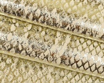 May include: Close-up of a gold metallic fabric with a snakeskin pattern. The fabric has a textured, distressed look.