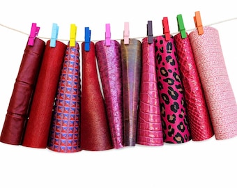 May include: Ten sheets of faux leather in various shades of red and pink, featuring textures like leopard print, crocodile skin, and geometric patterns, are hung on a string with colorful plastic clothespins against a plain white background.