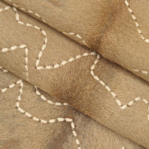 May include: Close-up of a brown cowhide rug with white stitching in a geometric pattern.