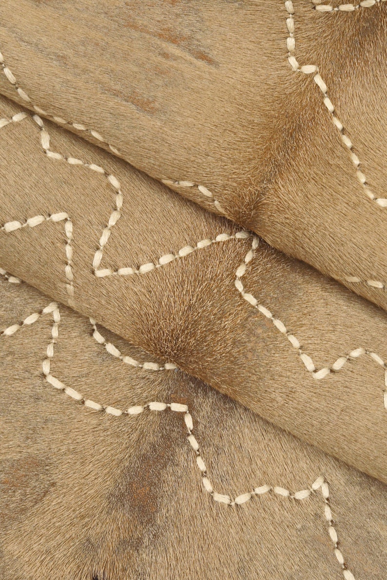 May include: Close-up of a brown cowhide rug with white stitching in a geometric pattern.