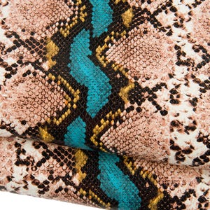 May include: Close-up of a snakeskin pattern in shades of tan, black, yellow, and turquoise. The design features a repeating scale pattern with a central turquoise stripe. The material appears to be folded over.