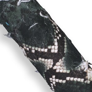 May include: Close-up of a dark green, textured material with a pattern of white and black squares. The material has a snake-like appearance. The text "Verde scuro" is at the bottom.