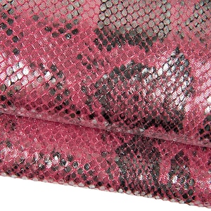 May include: Close-up of a textured fabric with a snakeskin pattern. The fabric is primarily a vibrant pink with silver and black accents, creating a shimmering effect. The word "Rosso" is visible at the bottom.
