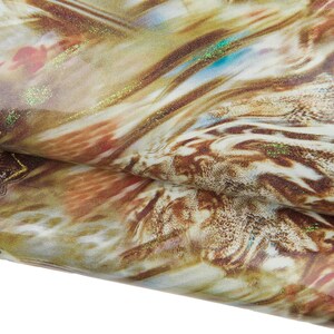 Op de afbeelding: Close-up van een gevouwen stof met een wervelend patroon in bruin-, beige- en goudtinten. De stof heeft een glinsterende, iriserende kwaliteit met hints van blauw en rood. Het ontwerp lijkt op een natuurlijke, organische textuur.
