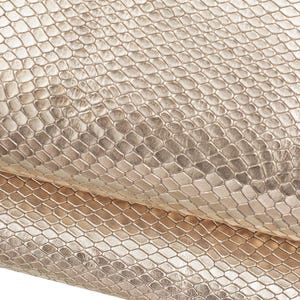 May include: A metallic gold material featuring a repeating embossed snakeskin texture. The surface displays a consistent pattern of small, raised hexagonal scales that create a reflective, shimmering appearance across the entire folded fabric.