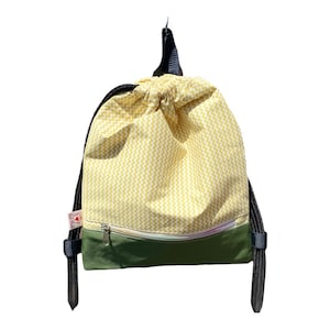 May include: A yellow and white chevron patterned drawstring backpack with a green bottom and a zippered pocket. The backpack has black drawstrings.