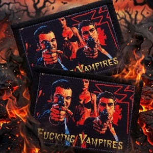 May include: A rectangular fabric patch featuring a graphic illustration of two men pointing handguns and a woman standing between them. The text "FUCKING VAMPIRES" is printed in yellow at the bottom against a dark background with red accents.