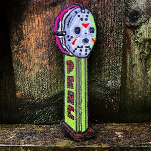 May include: Embroidered patch featuring a hockey mask design with pink, white, and black accents. The patch has a green base with the word "PEZ" in red letters. The patch is a novelty item.