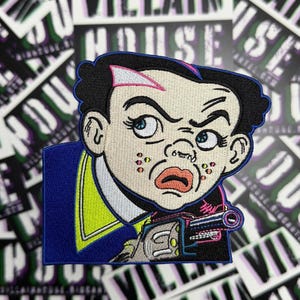 May include: Embroidered patch featuring a cartoon character with a stern expression, holding a gun. The character has black hair, blue eyes, and a blue suit with a yellow collar. The patch is bordered in blue and has the text "VILLAIN HOUSE" in the background.