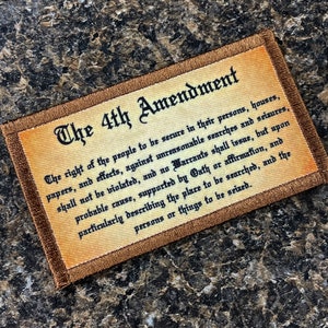 Può includere: Una toppa rettangolare con il testo "The 4th Amendment" in un carattere decorativo. Il testo dell'emendamento è stampato in nero. La toppa ha uno sfondo beige con un bordo marrone.