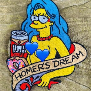 Puede incluir: Un parche bordado con un personaje de dibujos animados amarillo con cabello azul, sosteniendo una lata de cerveza y una dona. El personaje lleva un collar rojo y tiene dos corazones azules en el pecho. El parche tiene una pancarta que dice "Homer's Dream".