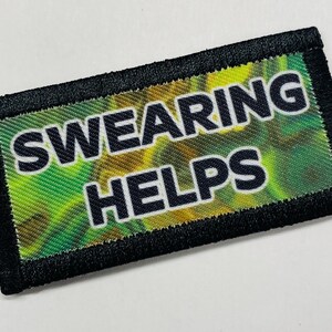 Può includere: Un cerotto ricamato nero e verde con il testo "SWEARING HELPS" in lettere bianche.