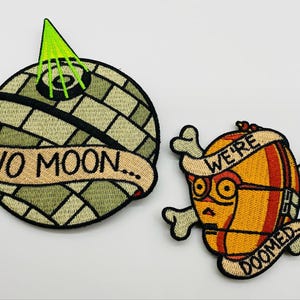 May include: Two embroidered patches. One is a planet with a green cone and the words "NO MOON...". The other is a yellow droid with the words "WE'RE DOOMED" and crossbones.