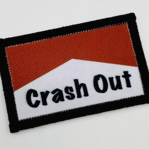 Peut inclure: Écusson brodé rectangulaire avec un motif rouge et blanc et l'inscription "Crash Out" en noir, bordé d'un cadre noir. Ce patch est conçu pour être cousu ou repassé sur des vêtements ou des accessoires, ajoutant un élément décoratif.