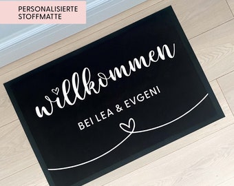 May include: Black welcome mat with white text that reads "Willkommen bei Lea & Evgeni" with a heart symbol on either side of the text.