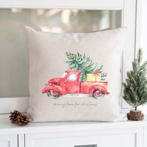Könnte beinhalten: Ein roter Vintage-Pickup mit einem Weihnachtsbaum und Geschenken in der Ladefläche. Der Truck fährt nach Hause zu Weihnachten. Das Bild ist auf einem beigefarbenen Leinenkissen.