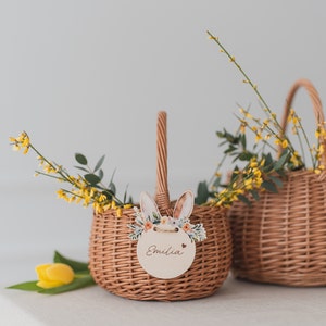 May include: Two wicker baskets with yellow flowers and a bunny-shaped tag with the name "Emilia" on one of the baskets.
