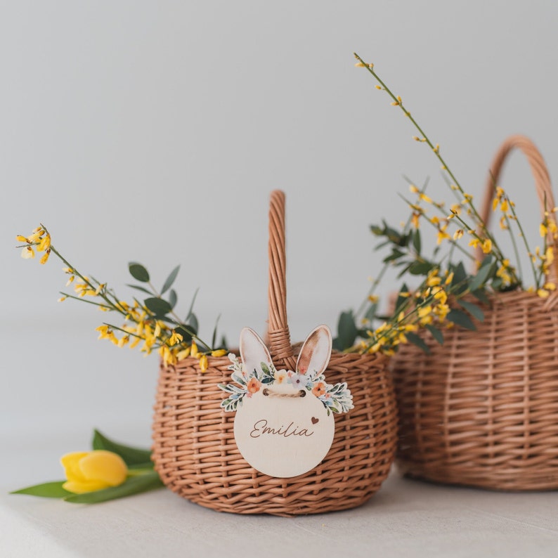 May include: Two wicker baskets with yellow flowers and a bunny-shaped tag with the name "Emilia" on one of the baskets.
