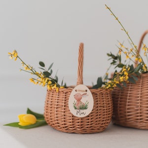 May include: Two brown wicker baskets with handles, one with a wooden tag that says "Mia" and has a cartoon bunny illustration. Both baskets are filled with yellow flowers.
