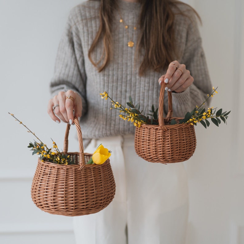 May include: Two brown wicker baskets with yellow flowers and a yellow tulip. The baskets have handles and are sitting on a white surface.