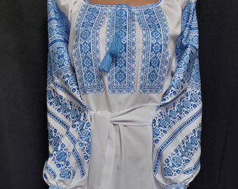 May include: A white embroidered dress with blue floral patterns and tassels. The dress has a long skirt and long sleeves.