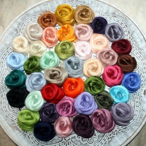 Könnte beinhalten: Eine Sammlung von 30 verschiedenen farbigen Seidenfasern, die in einem Kreis auf einem weißen Teller mit einem dekorativen Muster angeordnet sind. Die Fasern haben alle die Form einer Rose.