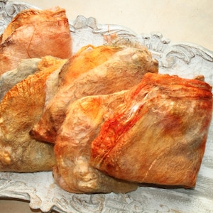 Könnte beinhalten: Fünf orangefarbene, gelbe und rote Filzwollstücke in einem dekorativen weißen Tablett. Die Wollstücke sind zu einem Stapel angeordnet, wobei das größte Stück oben liegt.