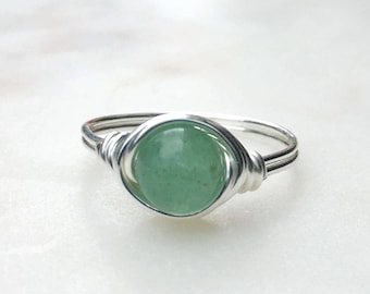 May include: A silver wire-wrapped ring featuring a round, light green gemstone. The gemstone is the focal point, held securely by the coiled wire. The ring has a simple, elegant design, suitable for everyday wear.