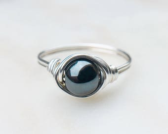 Könnte beinhalten: Ein silberner Ring mit einem schwarzen Edelstein, der in Draht gewickelt ist.