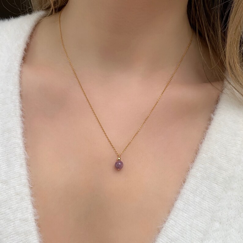 May include: A delicate gold chain necklace with a small, round, purple gemstone pendant.
