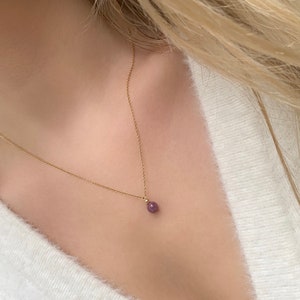 May include: A delicate gold chain necklace with a small, round, purple gemstone pendant.