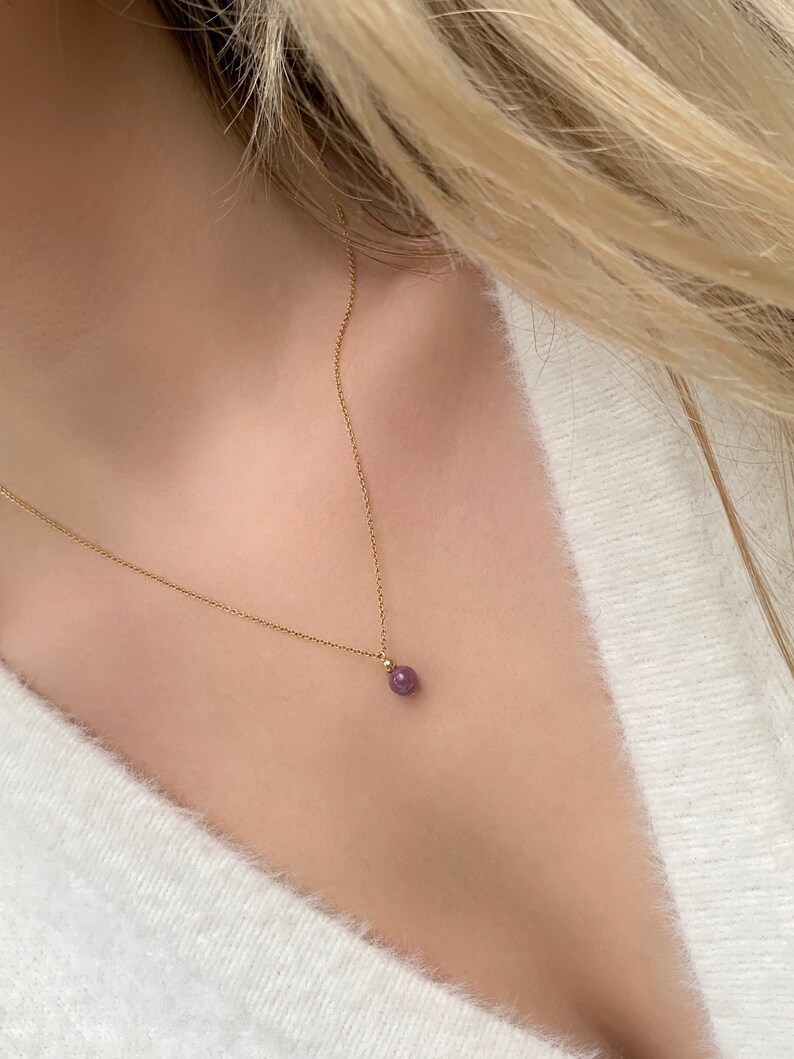 May include: A delicate gold chain necklace with a small, round, purple gemstone pendant.