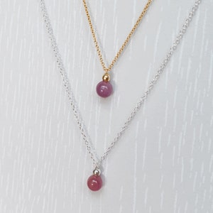 May include: Two necklaces with a pink gemstone pendant. The top necklace has a gold chain and the bottom necklace has a silver chain.