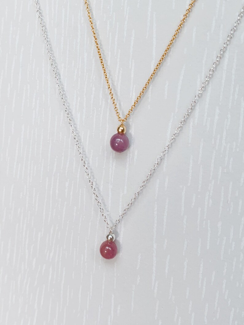 May include: Two necklaces with a pink gemstone pendant. The top necklace has a gold chain and the bottom necklace has a silver chain.