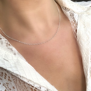 May include: A silver chain necklace worn on a person's neck. The chain is thin and delicate.