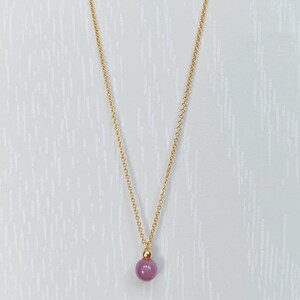 May include: A gold chain necklace with a single, round, purple gemstone pendant.