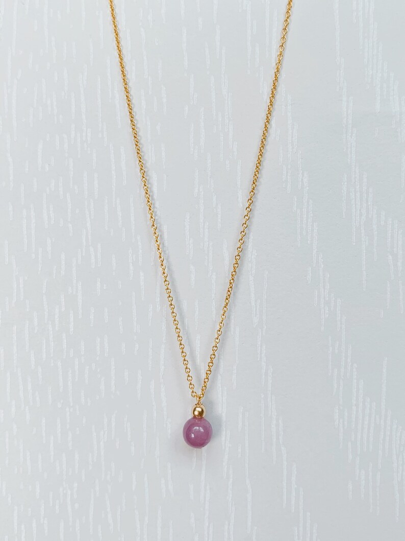 May include: A gold chain necklace with a single, round, purple gemstone pendant.