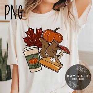 May include: A white t-shirt with a fall-themed design featuring a squirrel, pumpkin, coffee cup, pie, and a leaf. The coffee cup says "Spice" on it.