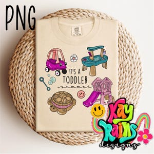 May include: Beige t-shirt with a colorful graphic of toddler toys, including a purple car, a water table, a playhouse with a slide, and a turtle. The text "IT'S A TODDLER summer" is also printed on the shirt.