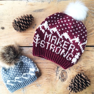 May include: Two knitted winter hats with pom poms. One hat is red with white accents and the text "Maker Strong". The other hat is blue with white accents.