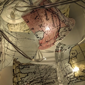 May include: String of lights with globe-shaped bulbs. Each bulb is covered in a vintage map print with a pink, cream and brown colour scheme. The lights are strung on a clear wire.