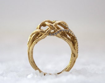 May include: A gold ring with a unique, intricate design featuring a woven, branch-like pattern accented with small, clear diamonds.