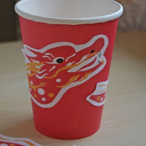 May include: A red paper cup with a white rim and a dragon design. The dragon is red and yellow with white accents. A matching dragon sticker is next to the cup. The text "MY PINK ERASER" is in the bottom right corner.