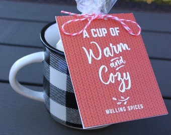 Puede incluir: Una etiqueta de regalo roja y blanca con el texto "A Cup of Warm and Cozy Mulling Spices" sobre un fondo rojo de punto. La etiqueta está atada con una cuerda a una taza a cuadros blancos y negros.